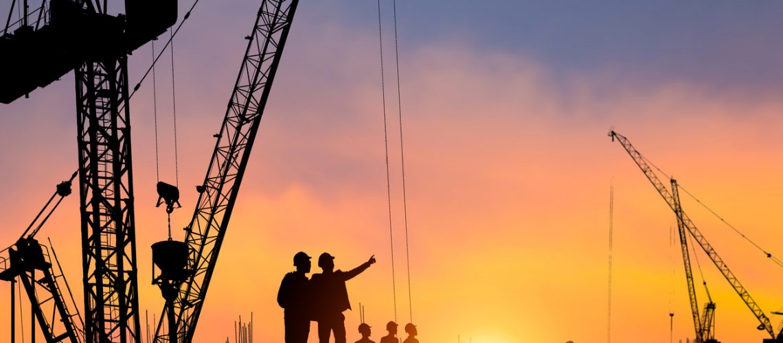 Silhouette of Engineer and worker checking project at construction site, building site with blurred sunset sky in evening time background