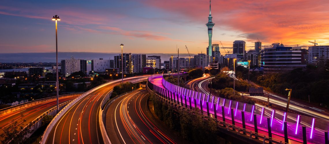 View of Auckland city skyline, Skytower, and motorway with car trails at sunrise.